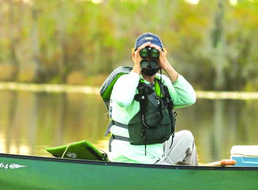 A visitor uses binoculars from a canoe in the Okefenokee Swamp